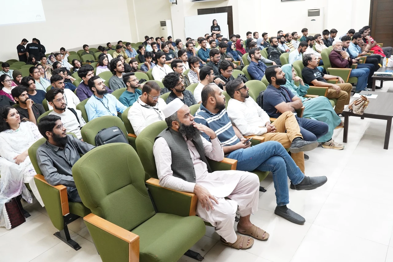 A full auditorium watches the Hacktoberfest presentation from rows of green seats.