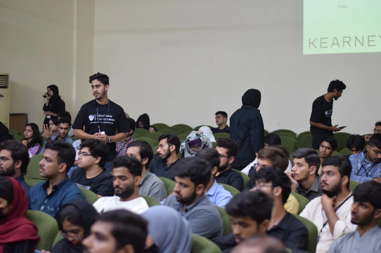 A person in a Cloud Native Security Lahore shirt stands among seated attendees.