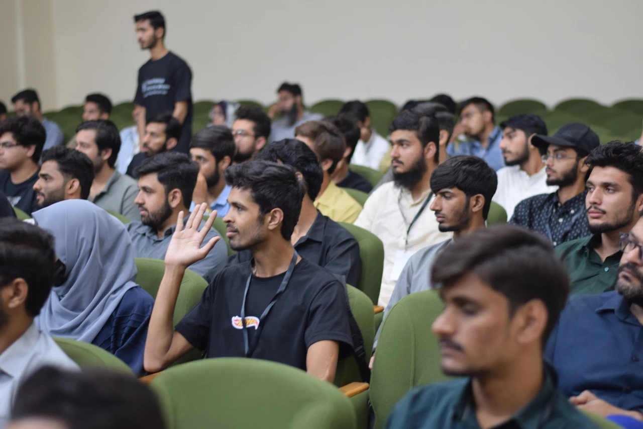 An audience member raises his hand while others watch the stage.