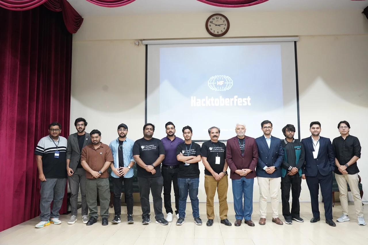 Speakers and organizers pose on stage in front of the Hacktoberfest screen.